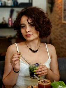 Young woman with curly hair enjoying a refreshing drink indoors at a cozy cafe.