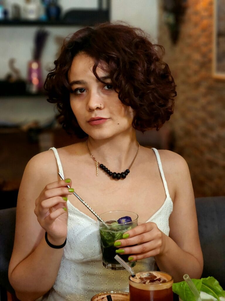 Young woman with curly hair enjoying a refreshing drink indoors at a cozy cafe.