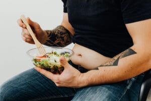 A tattooed individual holding a fresh salad, symbolizing healthy lifestyle and fitness motivation.