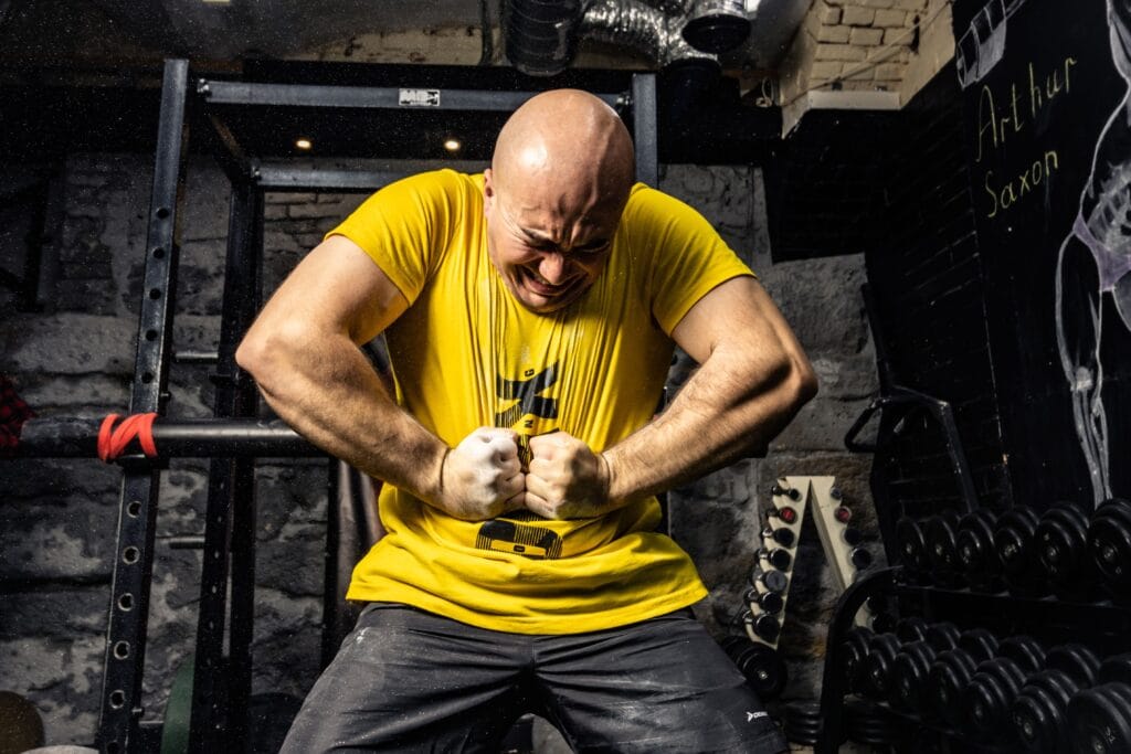 Bald muscular man in yellow t-shirt showcasing strength in a gym, highlighting intense dedication.