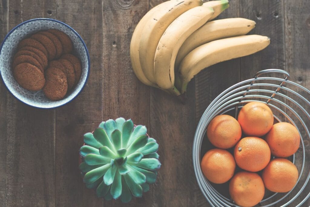 A rustic table setting featuring bananas, oranges, cookies, and a succulent plant.