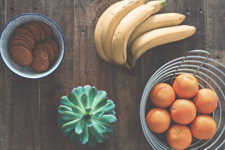 A rustic table setting featuring bananas, oranges, cookies, and a succulent plant.