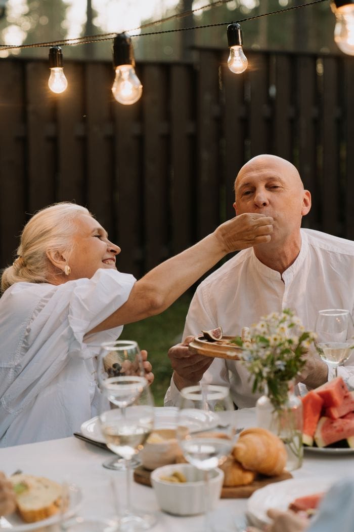 Elderly couple sharing a happy dining moment outdoors with warm lighting and delicious food.
