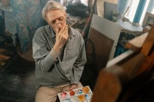 Senior artist in a cozy workshop, deep in creative thought.