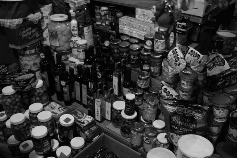 A black and white photograph showcasing a variety of packaged and bottled food items in a market setting.