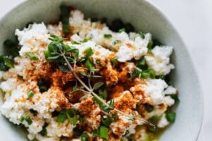 Top view of bowl with healthy salad with cottage cheese green onion and brunch of thyme placed on table in kitchen