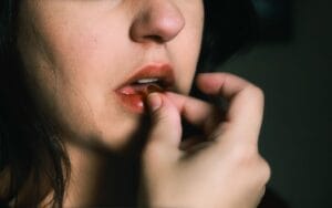 A close-up image of a woman placing a pill on her lips, indoors.