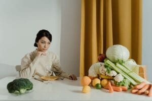 A woman seated at a table with a variety of fresh vegetables, representing healthy eating.