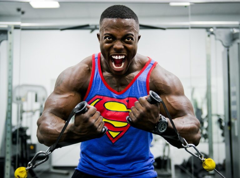 muscular man wearing a superman tanktop doing a post-failure method cable exercise