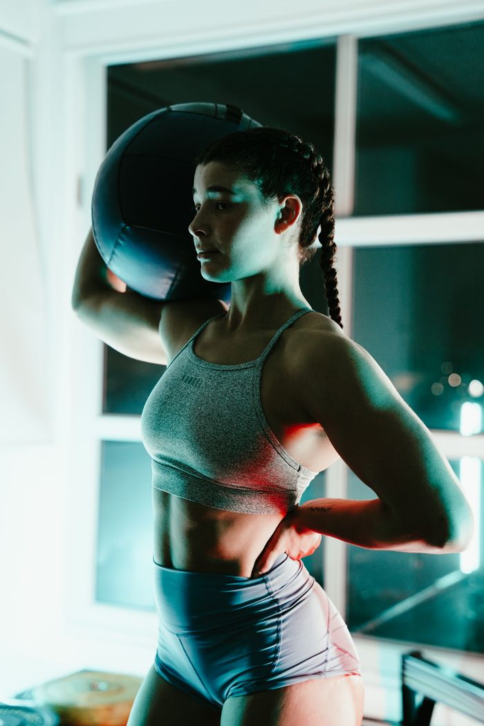 Fit woman in sportswear posing with a medicine ball in an indoor setting, showcasing strength and determination.