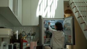 A woman in pajamas checks the refrigerator in a warmly lit cozy kitchen.