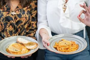 Two women presenting stylish plates of appetizing pasta and bread for a delightful dining experience.