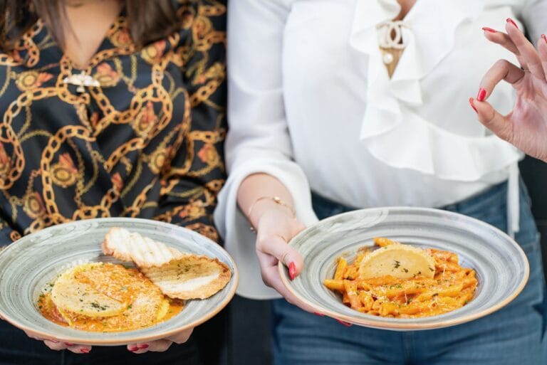 Two women presenting stylish plates of appetizing pasta and bread for a delightful dining experience.