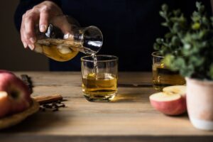 Close-up of someone pouring apple cider vinegar into a glass on a wooden table with apples and spices.