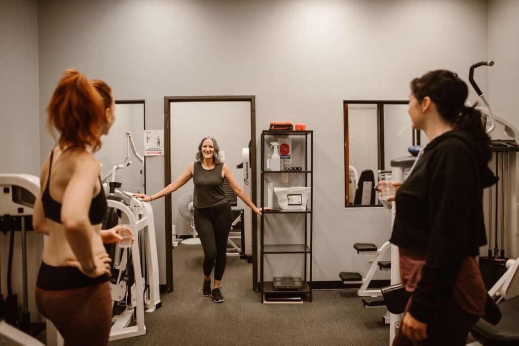 Three women in a gym setting focus on fitness and wellness after midlife.