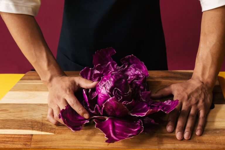 Close-up of hands holding fresh red cabbage on a wooden cutting board.